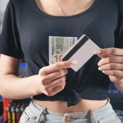Kobieta trzyma banknot 100 dolarów i kartę płatniczą, zastanawiając się, ile można wyplacic w Żabce.