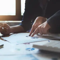 Dwie osoby analizują wykresy, gdy bank zgłasza wyłudzenie kredytu. Na stole leżą dokumenty, okulary i długopis.