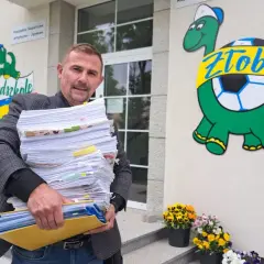Mężczyzna z dużą stertą dokumentów przed żłobkiem z logo żółwia.