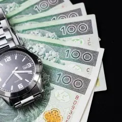 Zegarek na stosie banknotów 100 zł. Czas na kredyt konsolidacyjny na chwilówki, by uporządkować finanse.