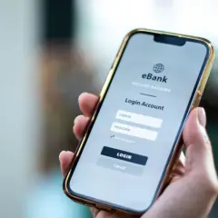 Dłoń trzyma smartfon z ekranem logowania do bankowości internetowej. Ktoś zapłacił moją kartą przez internet, muszę to sprawdzić.