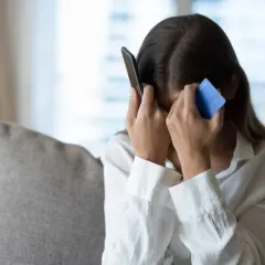 Zrozpaczona kobieta z kartą płatniczą i telefonem, ofiara oszustwa na wnuczka.