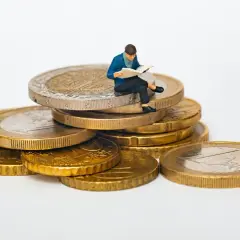 Figurka siedzi na stosie monet, czytając. Jak sprawdzić ile ktoś ma długu? Może warto zacząć od analizy finansów, jak ta figurka analizuje swoje monety.