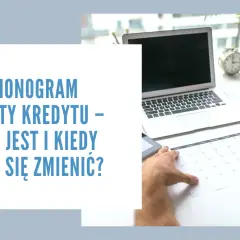 Ręka z fioletowym długopisem zaznacza datę w harmonogramie spłaty kredytu. Obok laptop, tablet i budzik.