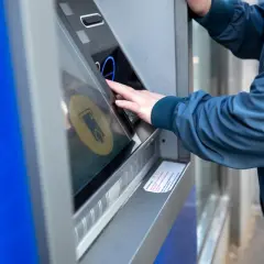 Osoba w granatowej kurtce korzysta z bankomatu, by dokonać żabka wypłata gotówki.