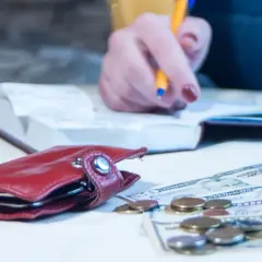 Kobieta notuje w zeszycie, obok leży portfel, monety i banknoty. To dobry moment, by sprawdzić swoje długi.