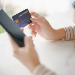 Kobieta trzyma kartę kredytową i telefon, przygotowując się do płatności online. Poznaj zasady bezpiecznego korzystania z karty.