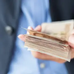 Dłoń trzymająca plik banknotów, ostrzeżenie przed oszustami w finansach dla ciebie.