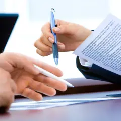 Dłonie trzymające długopisy nad dokumentami, symbolizujące analizę finansową.