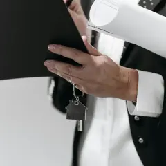 Dłoń trzymająca teczkę, klucze z brelokiem w kształcie domu i zwinięty dokument.