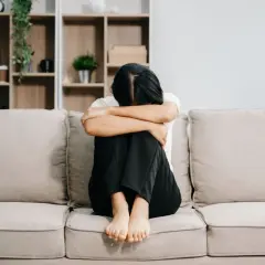 Kobieta siedzi skulona na kanapie, pogrążona w smutku po tym, jak jej mąż wziął kredyt bez zgody żony i zmarł.