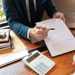 Doradca omawia z klientem dokumenty, porównując kredyt gotówkowy a hipoteczny. Na biurku kalkulator, notatniki i model domu.