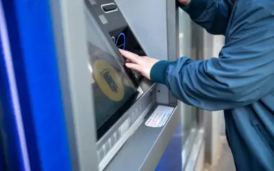Osoba w granatowej kurtce korzysta z bankomatu, by dokonać żabka wypłata gotówki.
