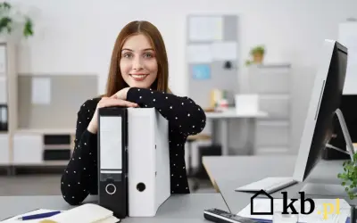 Uśmiechnięta kobieta w biurze opiera się o segregator.