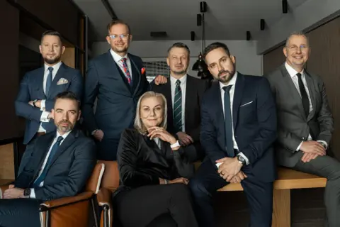 Grupa siedmiu profesjonalistów w garniturach, pozujących do zdjęcia w biurze.