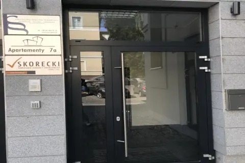 Drzwi wejściowe do budynku z tabliczkami informacyjnymi, w tym "SKORECKI KANCELARIA DORADCY FINANSOWEGO".