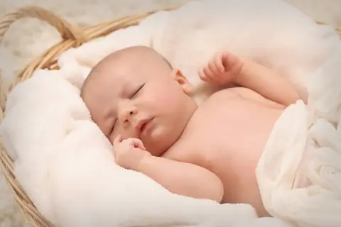 Śpiące dziecko w koszyku, otulone białym kocem.