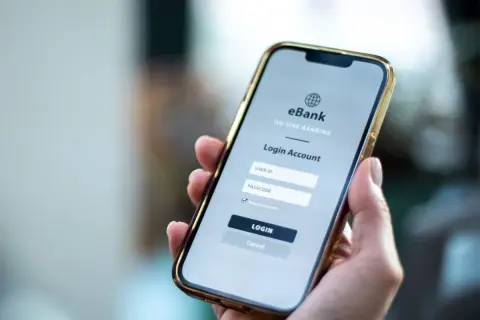 Dłoń trzyma smartfon z ekranem logowania do bankowości internetowej. Ktoś zapłacił moją kartą przez internet, muszę to sprawdzić.