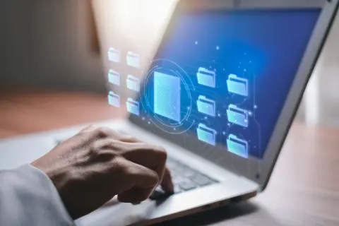 Dłoń na klawiaturze laptopa, wirtualne foldery i dokumenty. Czy raport BIK jest darmowy? Sprawdź online.