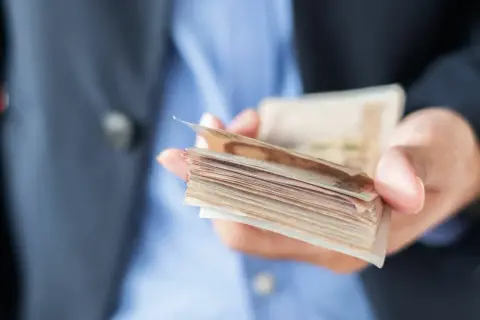 Dłoń trzymająca plik banknotów, ostrzeżenie przed oszustami w finansach dla ciebie.