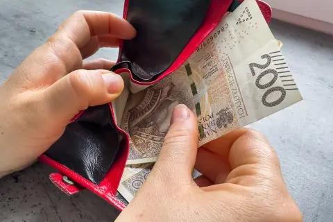 Dwie ręce wkładają banknot 200 zł do czerwonego portfela. Czy kosiniakowe wlicza się do dochodu?