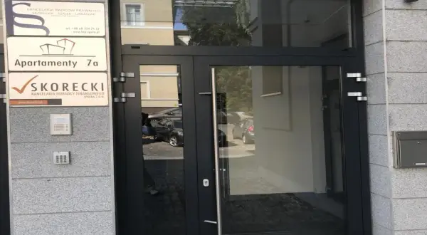 Drzwi wejściowe do budynku z tabliczkami informacyjnymi, w tym "SKORECKI KANCELARIA DORADCY FINANSOWEGO".