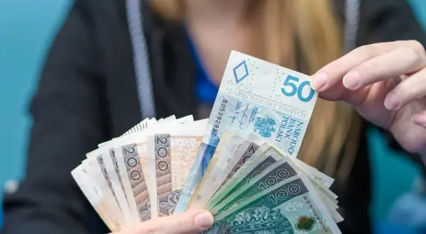 Dłoń trzyma plik polskich banknotów: 50, 100 i 200 zł. Może to być oferta kredytu w Revolut.