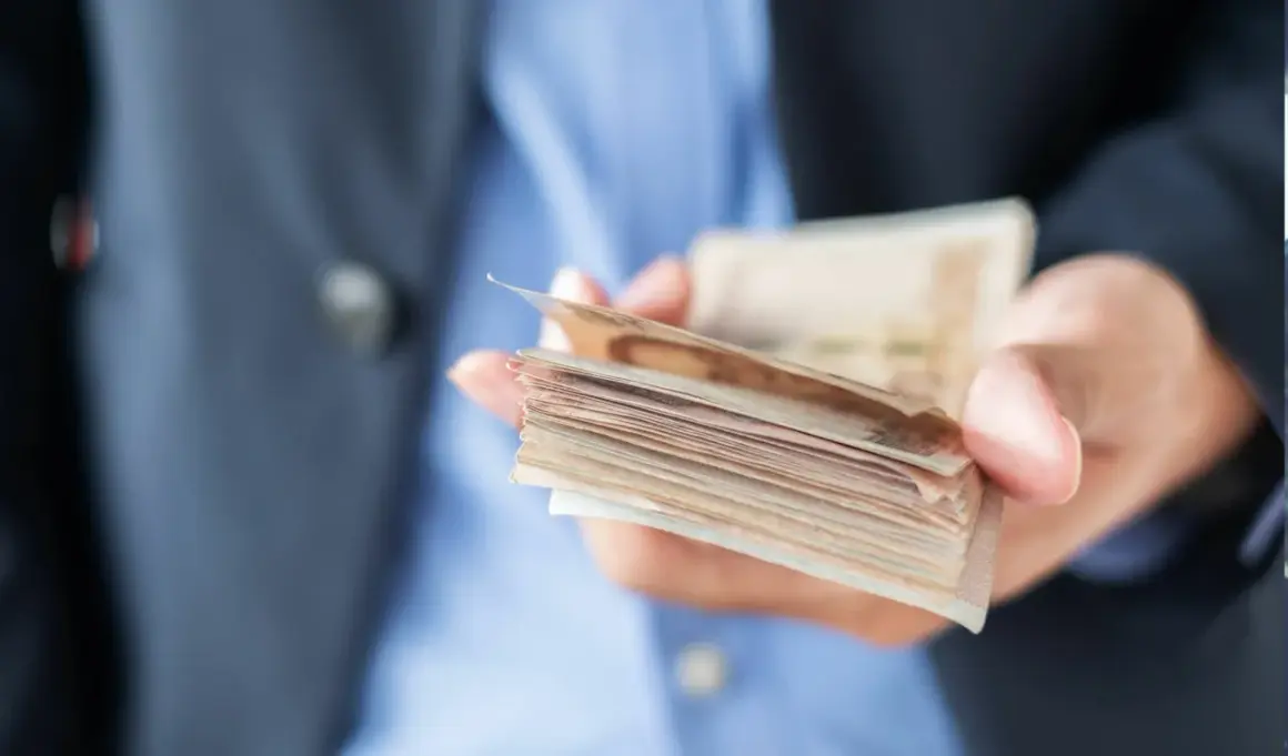 Dłoń trzymająca plik banknotów, ostrzeżenie przed oszustami w finansach dla ciebie.