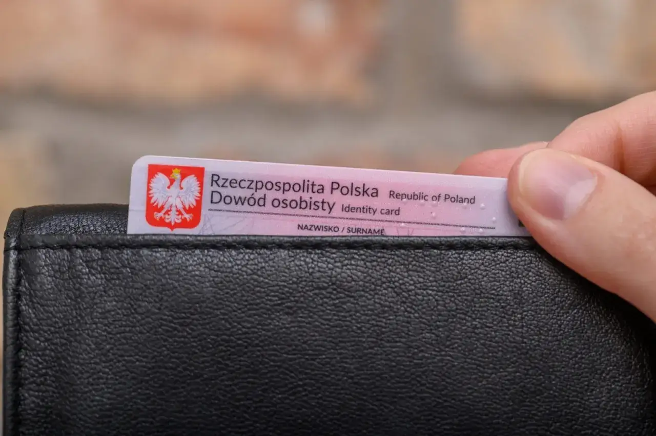 Dłoń wkłada do czarnego portfela polski dowód osobisty. Czy jest obowiązek noszenia dowodu osobistego?