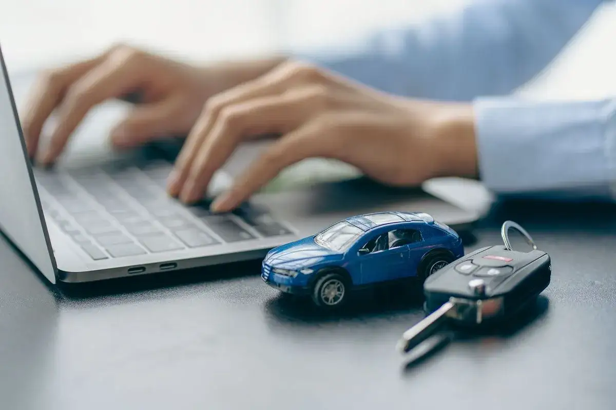 Ręce piszą na laptopie, obok niebieski model samochodu i kluczyki. To może być szukanie informacji o kredyt samochodowy oprocentowanie.