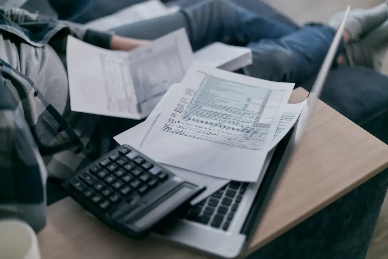 Osoba analizuje dokumenty, kalkulator i laptop, zastanawiając się, po jakim czasie przedawniają się długi bankowe.