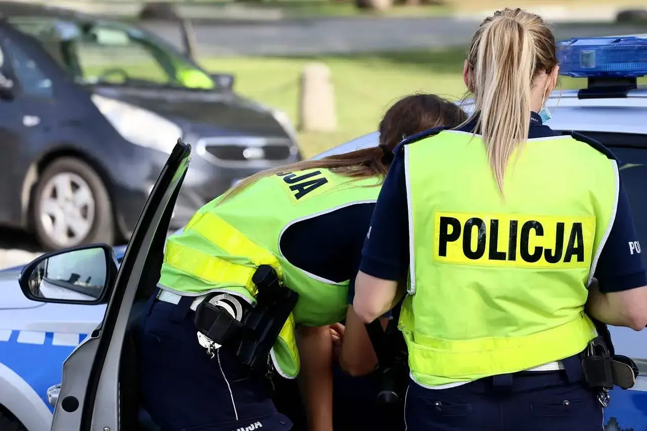 Policjantki w kamizelkach z napisem POLICJA przy radiowozie. Czy policjant może zabrać dowód osobisty do radiowozu?