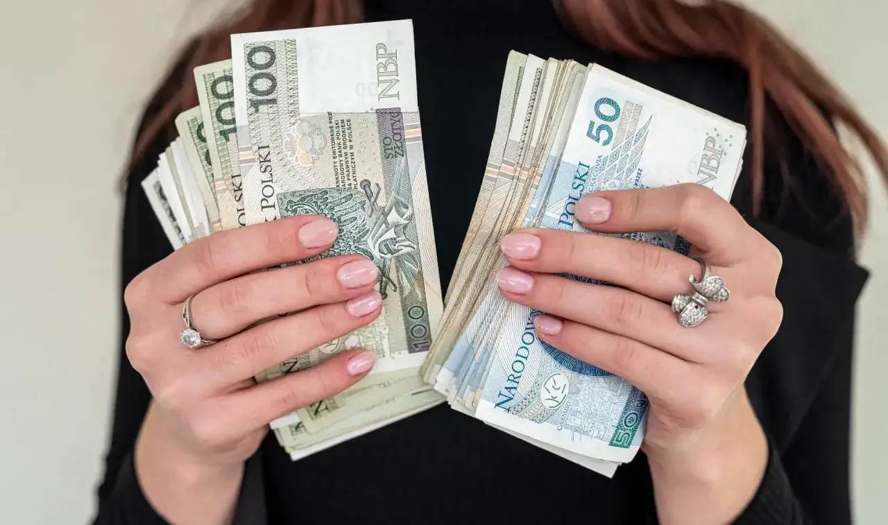 Dłonie trzymające pliki banknotów 100 i 50 zł. Czy to sposób na zakup sprzętu na raty dla zadłużonych?