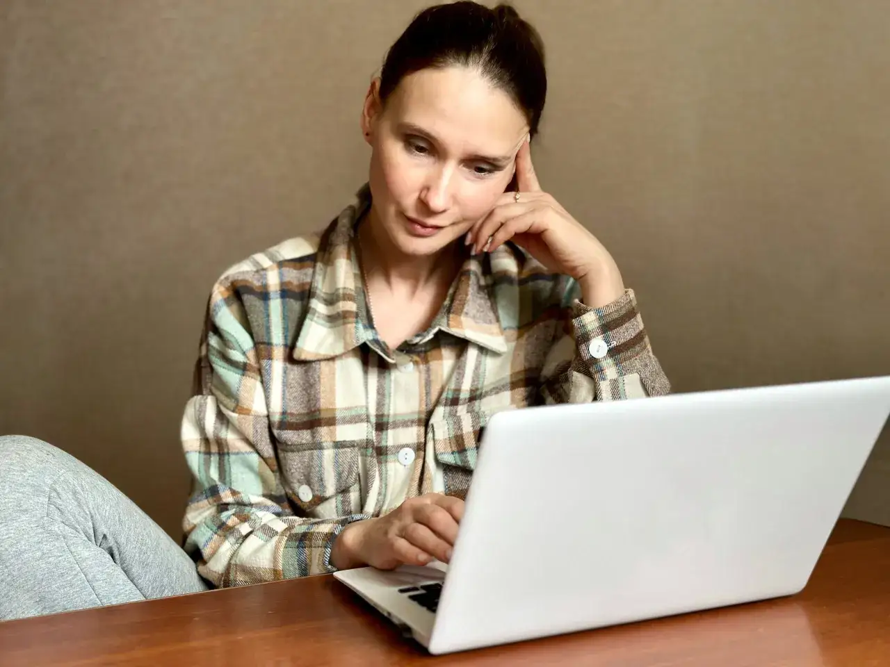 Kobieta w kratę szuka w internecie informacji, jak usunąć negatywny wpis w BIK, zamyślona nad rozwiązaniem problemu.
