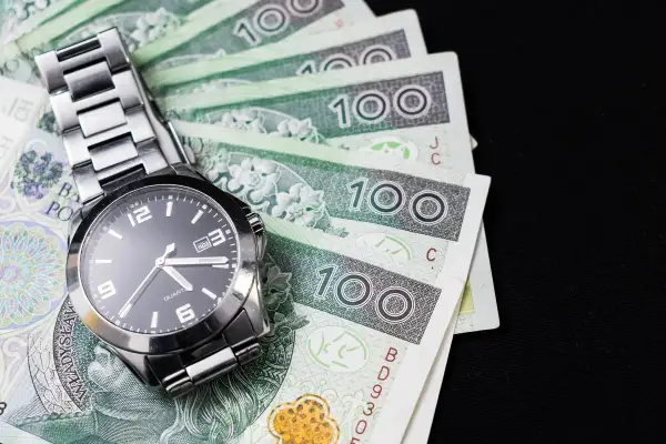 Zegarek na stosie banknotów 100 zł. Czas na kredyt konsolidacyjny na chwilówki, by uporządkować finanse.