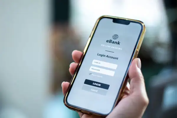 Dłoń trzyma smartfon z ekranem logowania do bankowości internetowej. Ktoś zapłacił moją kartą przez internet, muszę to sprawdzić.