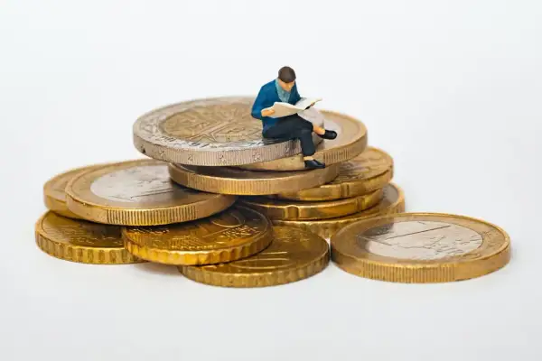 Figurka siedzi na stosie monet, czytając. Jak sprawdzić ile ktoś ma długu? Może warto zacząć od analizy finansów, jak ta figurka analizuje swoje monety.