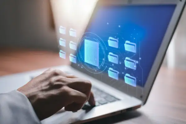Dłoń na klawiaturze laptopa, wirtualne foldery i dokumenty. Czy raport BIK jest darmowy? Sprawdź online.