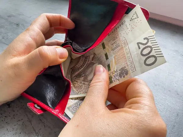 Dwie ręce wkładają banknot 200 zł do czerwonego portfela. Czy kosiniakowe wlicza się do dochodu?